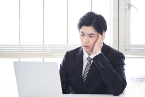 パソコンを見ながら悩んでいる男性実業家の画像